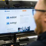 En medarbejder hos Mobitel arbejder ved en computerskærm, der viser virksomhedens løsninger inden for Product Business Lifecycle (PBC) og Life Cycle Management