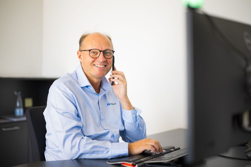 Mand i skjorte taler i telefon og arbejder ved computer – bliv kunde hos Mobitel