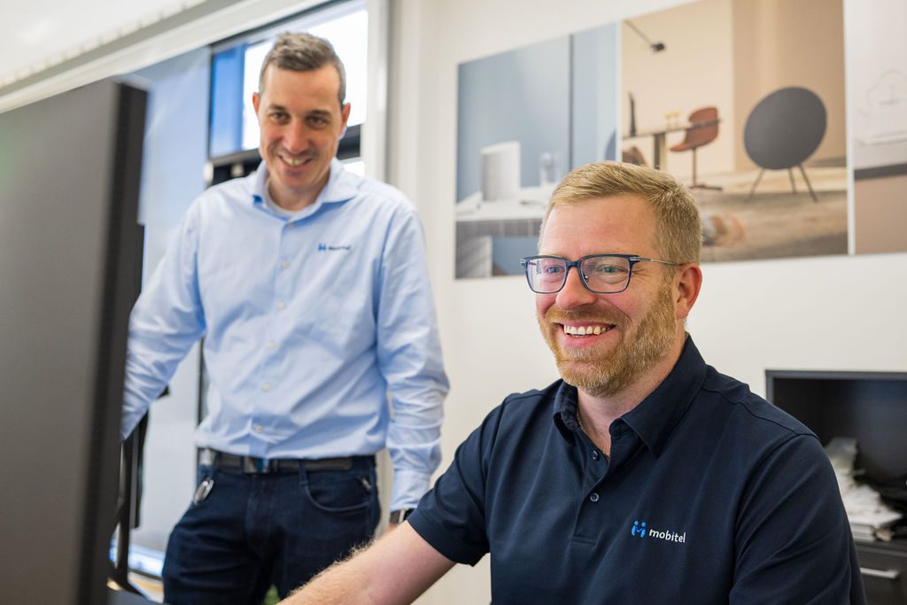 To become a Mobitel customer: two smiling men in an office setting.